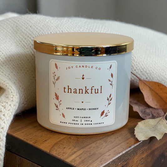 Thankful apple maple honey soy candle on a wooden table with a cozy knit blanket and fall leaves