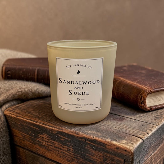 Sandalwood and Suede 12 oz candle with leather books on a wooden table
